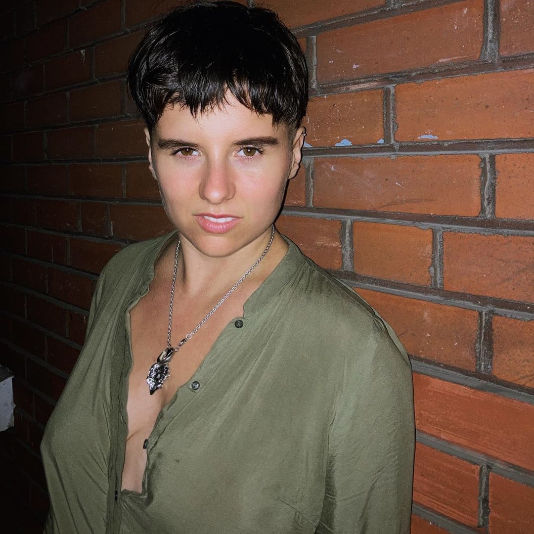 Angelica Poversky headshot wearing green shirt and leaning against a brick wall